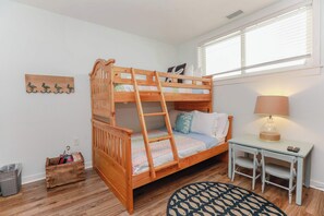 A bunk bed with a ladder, a small table with a lamp, and a wall-mounted shelf with decorative items.