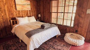A wooden room with a bed, a window with blinds, a rug, and a small round bed on the floor. - Room 2 • Cozy Desert Studio  - Downtown Joshua Tree (Joshua Tree)