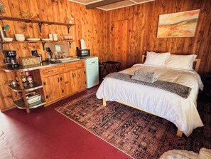 A wooden cabin-style room with a bed, a small kitchenette, and a rug. - Room 2 • Cozy Desert Studio - Downtown Joshua Tree (Joshua Tree)