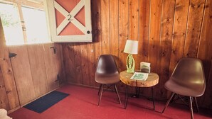 A room with wooden walls, a red carpet, two chairs, a small table with a lamp, and a barn-style number sign. - Room 2 • Cozy Desert Studio  - Downtown Joshua Tree (Joshua Tree)