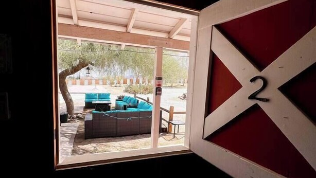 A room with a large window revealing an outdoor seating area with a sofa and a table. - Room 2 • Cozy Desert Studio  - Downtown Joshua Tree (Joshua Tree)