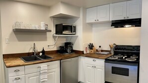 A modern kitchen with white cabinets, a stainless steel stove, a microwave, and a coffee maker. - Cosy Hideaway in the Heart of Tofino (Tofino)