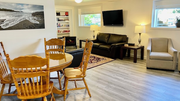 A living room with a dining area, a fireplace, a flat-screen TV, and a large window. - Cosy Hideaway in the Heart of Tofino (Tofino)