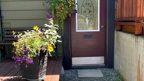 A wooden bench, a potted plant with flowers, a door with a number sign, and a wooden fence. - Cosy Hideaway in the Heart of Tofino (Tofino)