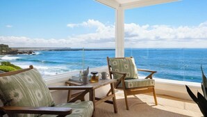 A room with a large window overlooking a beach and ocean, furnished with a table, chairs, and a coffee pot.