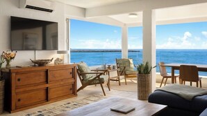 A spacious living area with a large TV, wooden furniture, and a view of the ocean.