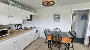Una cocina con armarios blancos, estufa, microondas y una mesa de comedor con sillas. Hay carteles en la pared y un candelabro sobre la mesa.