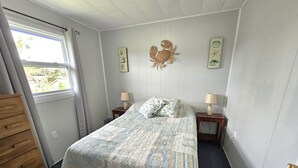Un dormitorio con cama, dos mesitas de noche, un aparador de madera y una ventana con cortinas.