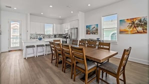 A modern kitchen with white cabinets, a central island, and a dining area with wooden chairs and a table.