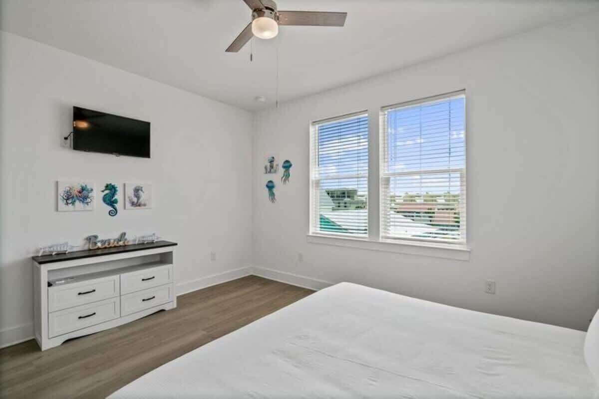A bedroom with a bed, a ceiling fan, a TV, and artwork on the wall.
