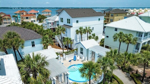 A residential area with a swimming pool surrounded by palm trees and houses with various roof colors.