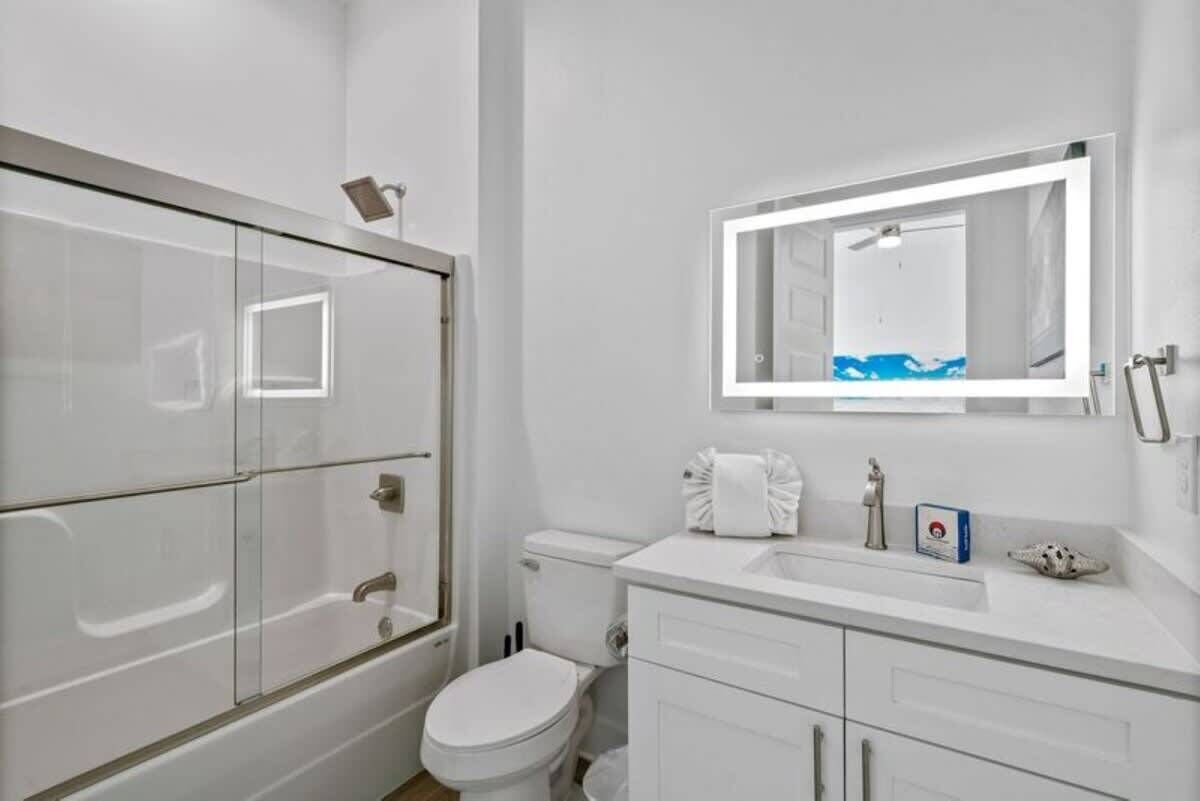 Une salle de bain moderne avec une douche à parois de verre, des toilettes blanches, un lavabo avec un miroir et un petit objet décoratif posé sur le comptoir.