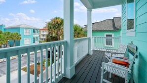A turquoise building with a porch featuring white railings and outdoor seating.