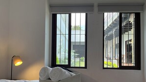 Hotelkamer met een bed, een bedlamp, een raam met uitzicht op een trap en buitenruimte, en een doos handdoeken op het bed.