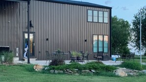 A modern building with a wooden exterior, a glass door entrance, outdoor seating with tables and chairs, and a landscaped garden area with rocks and plants. - Outdoor Oasis and Pickleball Paradise: Fishing, Paddle-boarding, Swimming (Augusta)