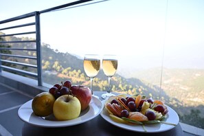 A table with two plates of fruit and two glasses of white wine, set against a scenic mountain view. - Amritara Kasauli kollections (Kasauli)