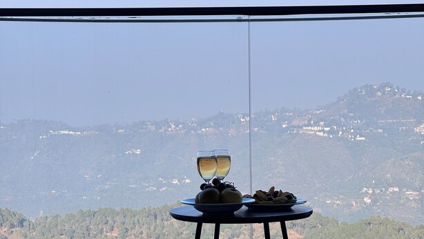 Ein Tisch mit zwei Weingläsern und einer Fruchtplatte in einem Raum mit einem großen Fenster mit Blick auf eine Berglandschaft.