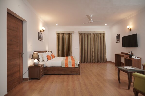 A bedroom with a bed, bedside table, lamp, curtains, a desk, chair, TV, and a ceiling fan.