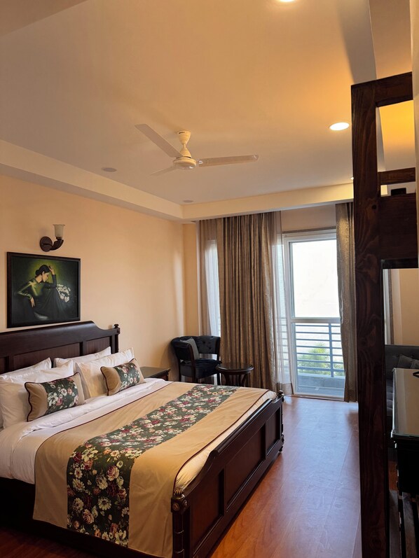 A hotel room with a large bed, a chair, a small table, a ceiling fan, and a window with curtains.