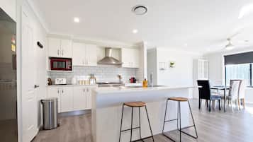 Una cocina moderna con armarios blancos, extractor de acero inoxidable y una isla central con taburetes.
