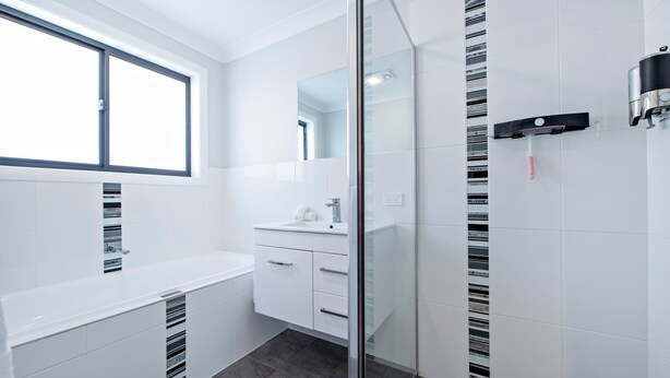 A modern bathroom with a glass shower enclosure, a white vanity with a sink, and a window above the vanity.