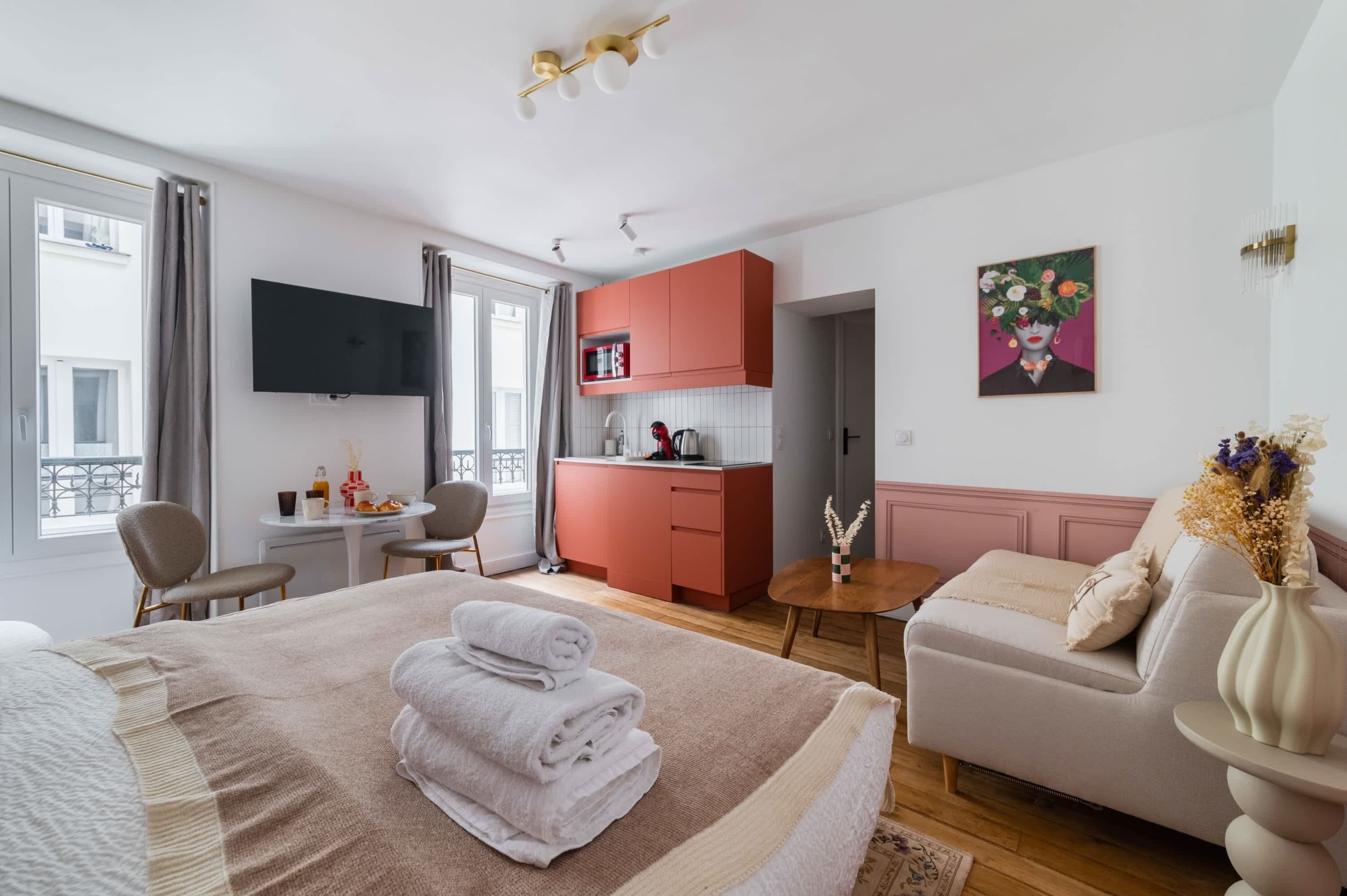 Een moderne hotelkamer met een bed, een slaapbank, een eettafel en een kitchenette.