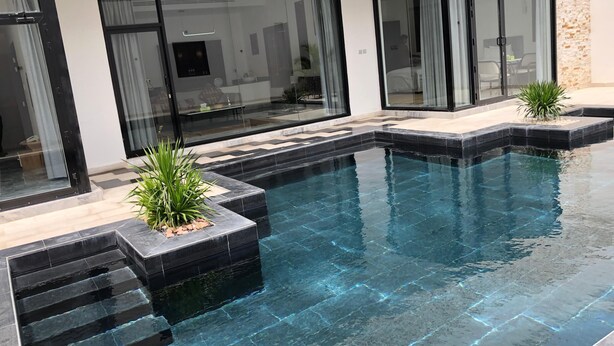 Una piscina moderna con agua cristalina, rodeada de baldosas negras y escalones.