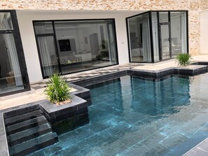 Una piscina moderna con agua cristalina, rodeada de baldosas negras y escalones.