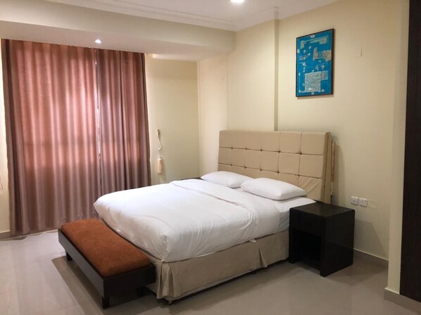 A hotel room with a large bed, a bedside table, a bench, and a wall-mounted information board. - The Palace Hotel Salalah (Salalah)