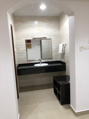 A bathroom with a white marble wall, a black countertop, a white sink, a mirror, and a towel rack. - The Palace Hotel Salalah (Salalah)