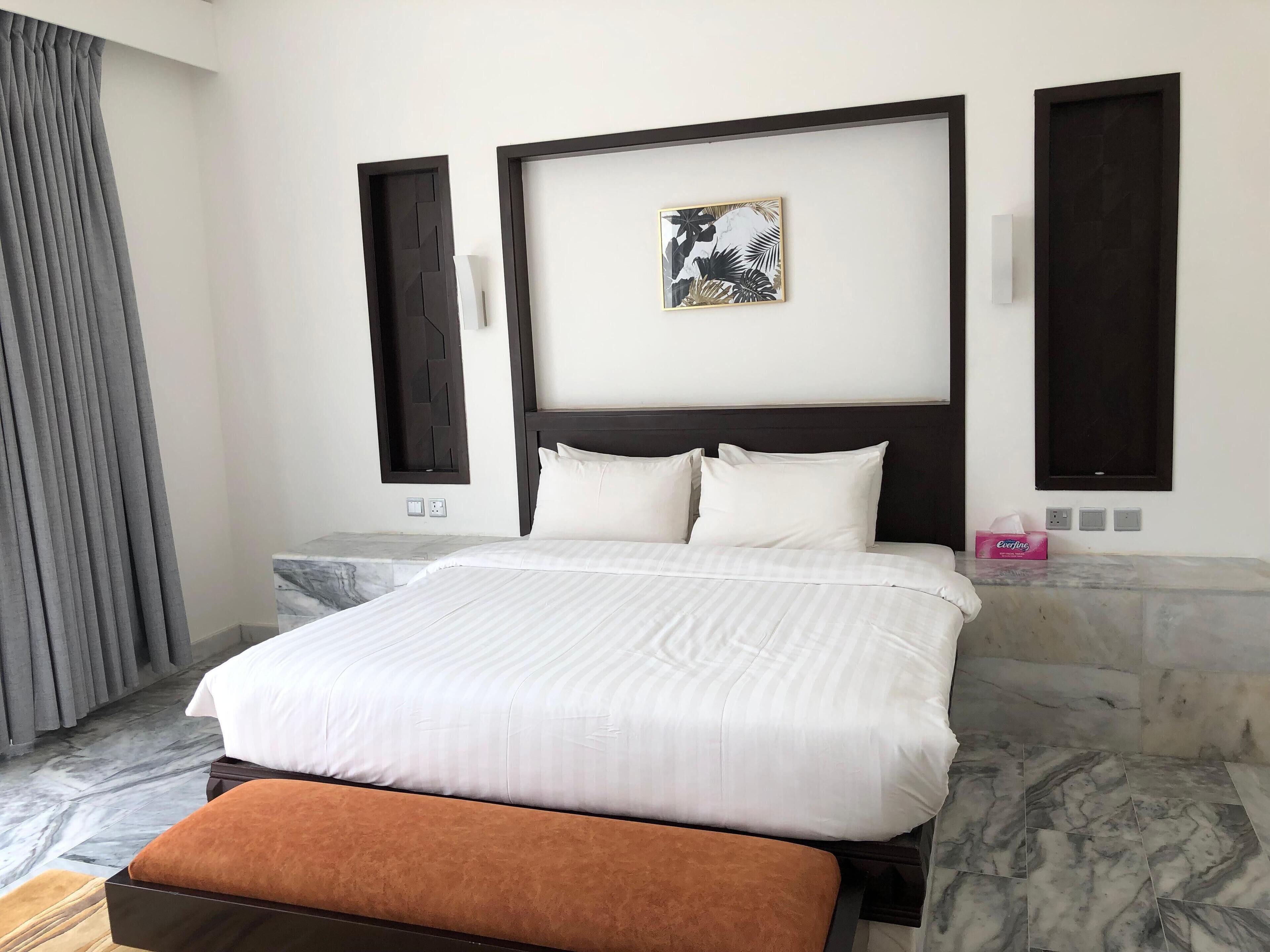 A hotel room with a large bed, a headboard, a framed picture on the wall, and a marble floor.