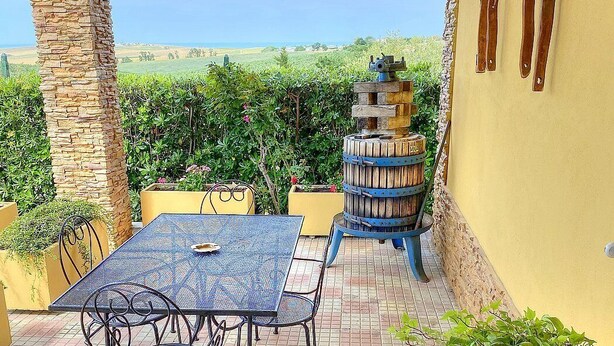 A patio with a table and chairs, a stone pillar, and a barrel.