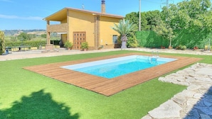 A house with a swimming pool surrounded by artificial grass and stone edging.