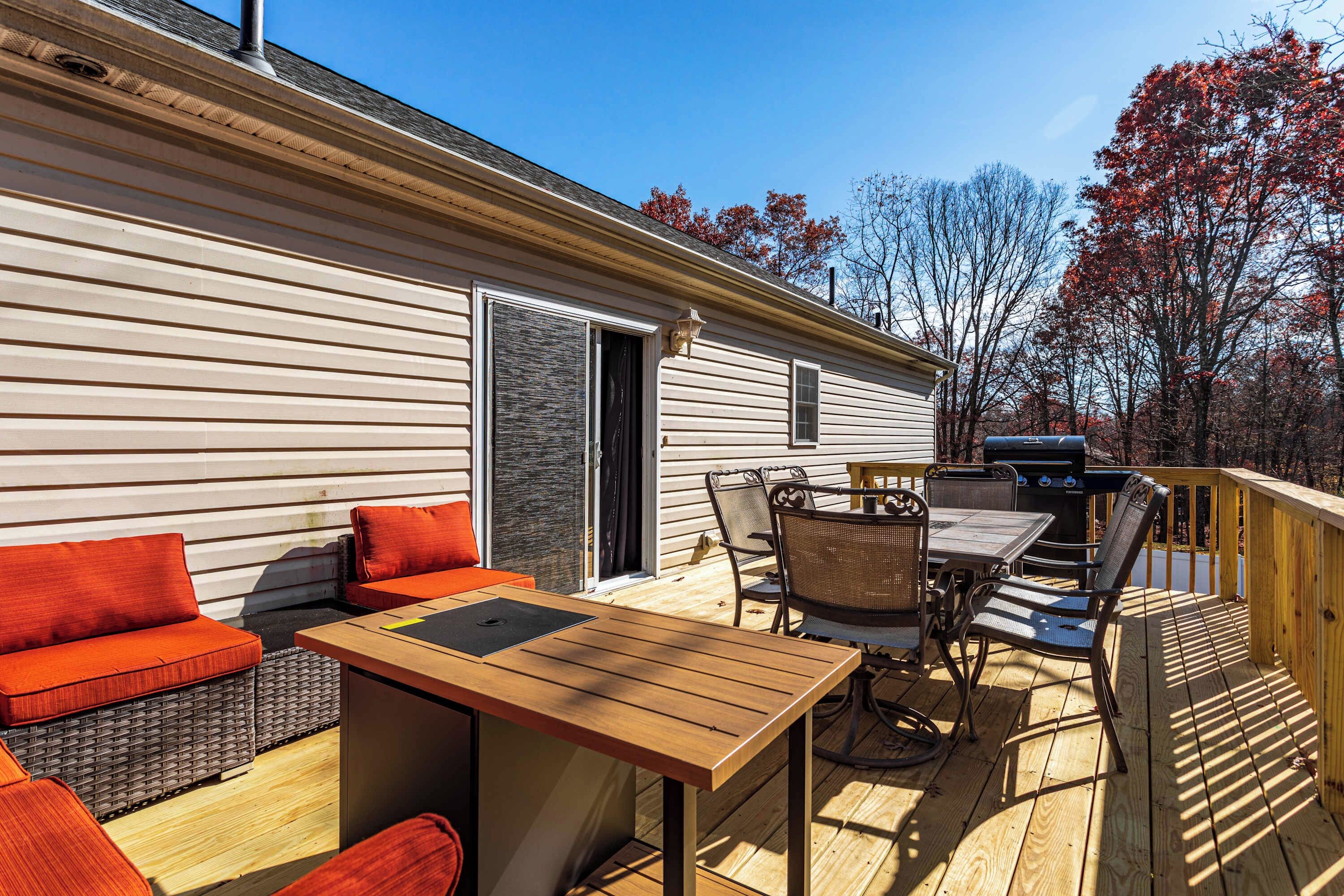 A deck with a wooden table and chairs, a sofa with orange cushions, and a grill.