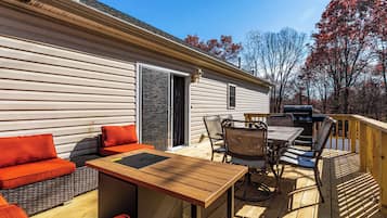 A deck with a wooden table and chairs, a sofa with orange cushions, and a grill.