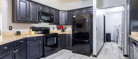 A modern kitchen with dark cabinetry, a black refrigerator, a microwave, and an oven.