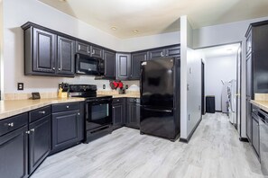A modern kitchen with dark cabinetry, a black refrigerator, a microwave, and an oven.