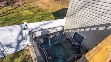 A hot tub adjacent to a house with a wooden deck and a white fence.