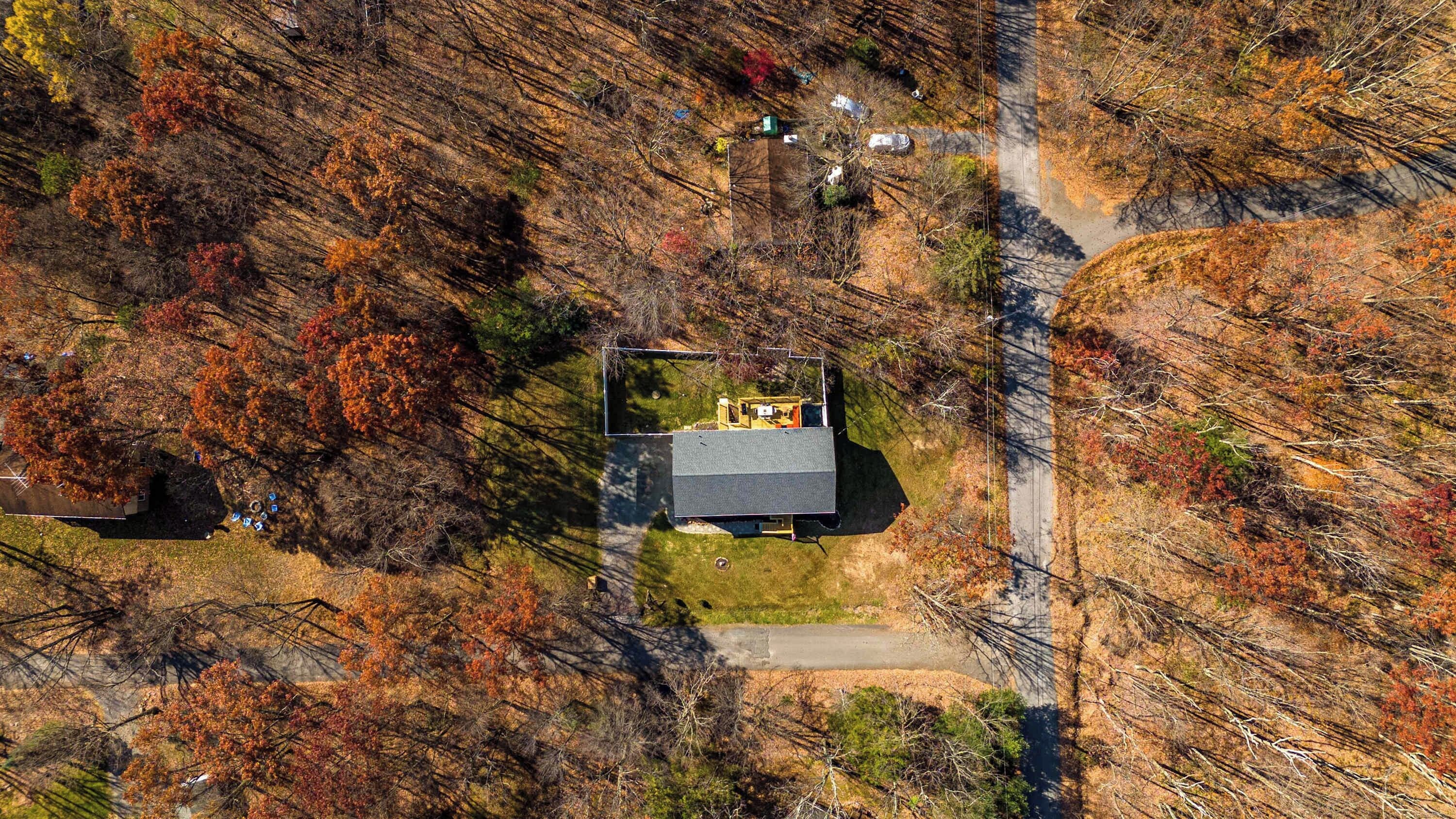 An aerial view of a house with a fenced yard, surrounded by trees with autumn foliage.