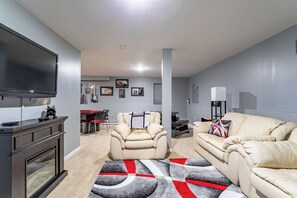 Een moderne woonkamer met een flatscreen televisie, beige banken, een open haard en een kamerkleed met een patroon.