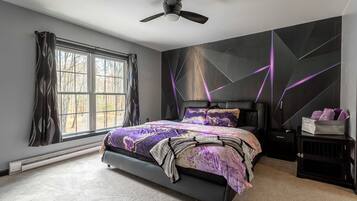 A bedroom with a bed, a ceiling fan, a window, and a wall with geometric patterns.