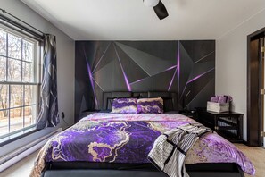 Une chambre moderne avec un grand lit, une fresque murale aux motifs géométriques et une fenêtre avec des rideaux.