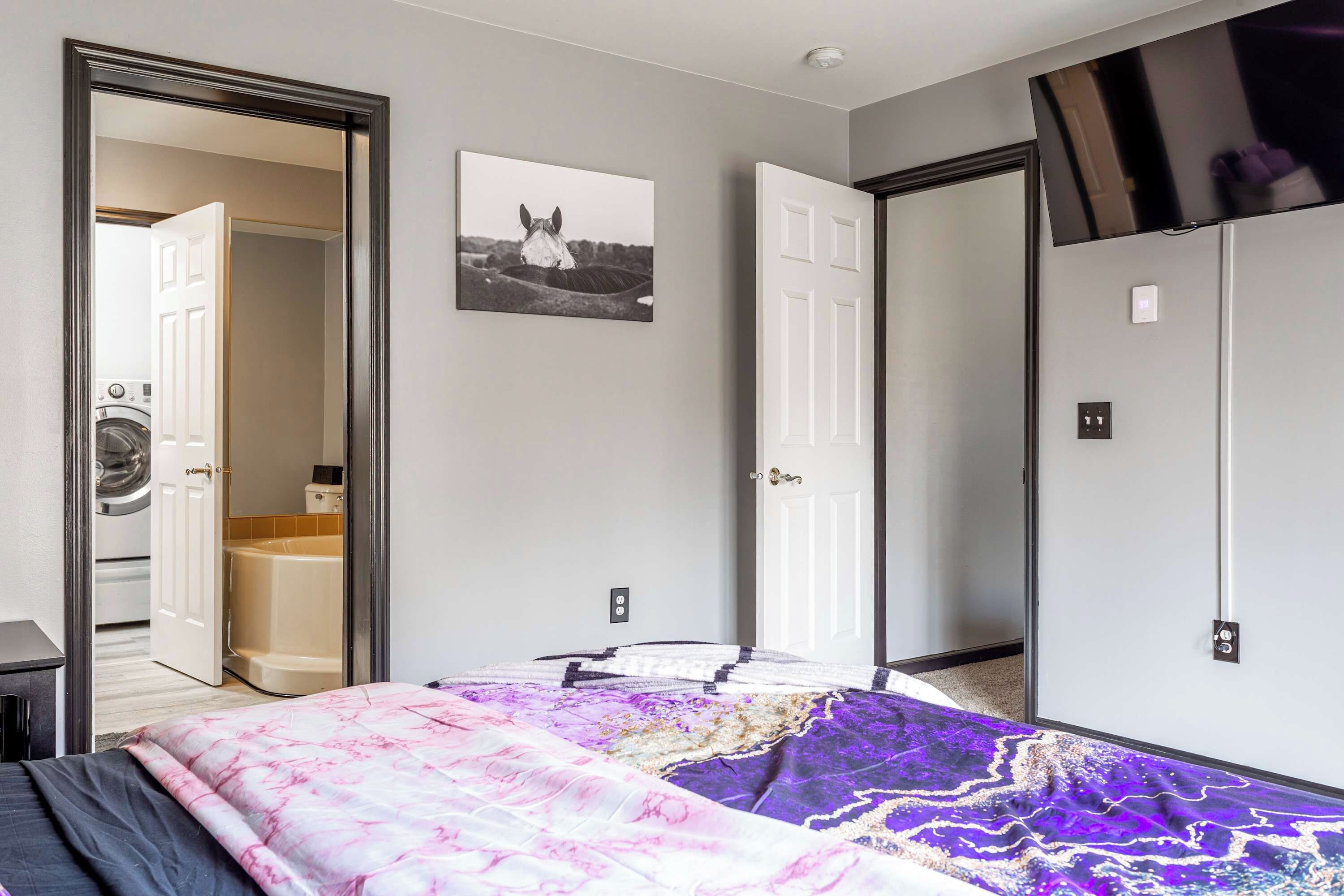 A bedroom with a bed, a door, a wall-mounted TV, and a framed picture.