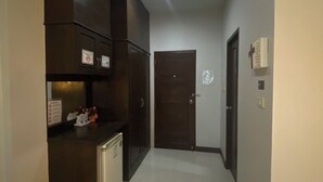 A narrow hallway with a kitchenette on the left, a door at the end, and a trash bin in the foreground. - Happyroom Airport Chiangrai (Chiang Rai)