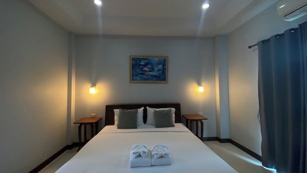 A hotel room with a large bed, two bedside tables, a painting on the wall, and a window with curtains. - Happyroom Airport Chiangrai (Chiang Rai)