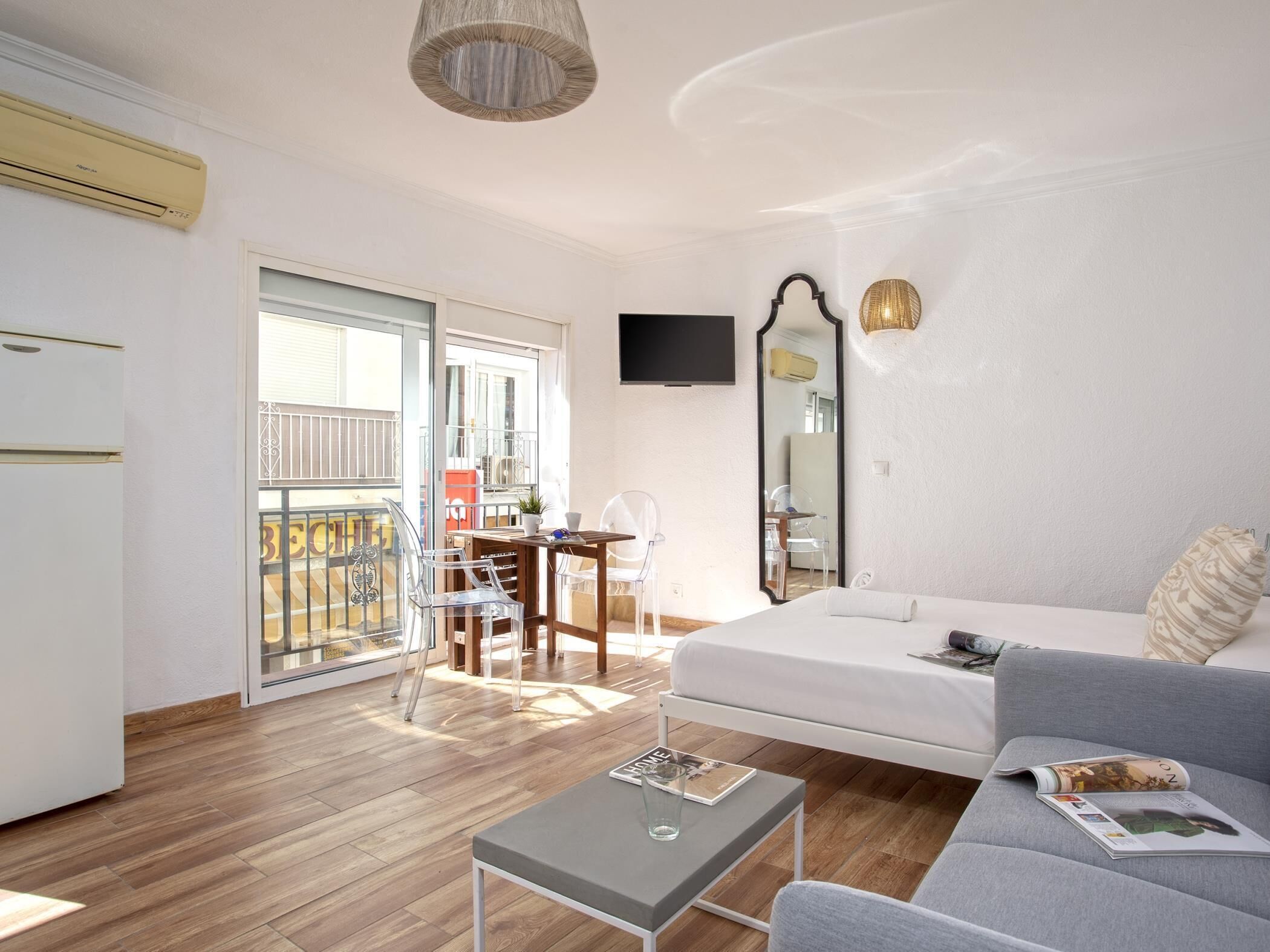 A modern living room with a sofa, a coffee table, and a TV. There is a balcony with a view of the outside.