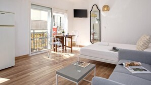 A modern living room with a sofa, a coffee table, and a TV. There is a balcony with a view of the outside.