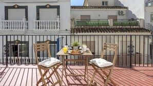 A terrace with two wooden chairs, a table with breakfast items, and a view of adjacent buildings.