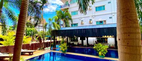 Piscina cercada por palmeiras e um edifício com várias janelas.