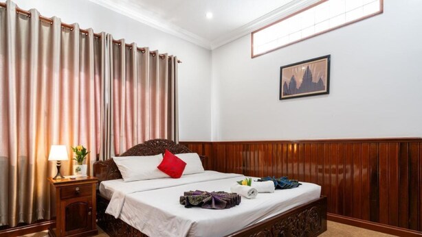 A hotel room with a wooden bed, a nightstand with a lamp, and a painting on the wall. - Cityhotel Siem Reap (Siem Reap)